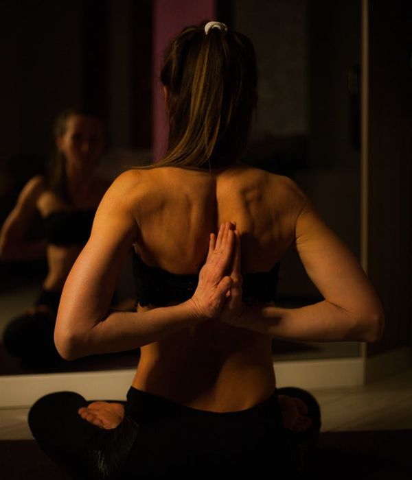 Woman in a calm, focused yoga pose against a dark background with light accents.